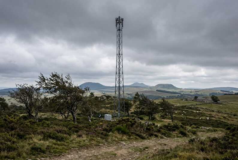 Antenne relais métallique installée dans un paysage de landes et de collines sous un ciel gris.