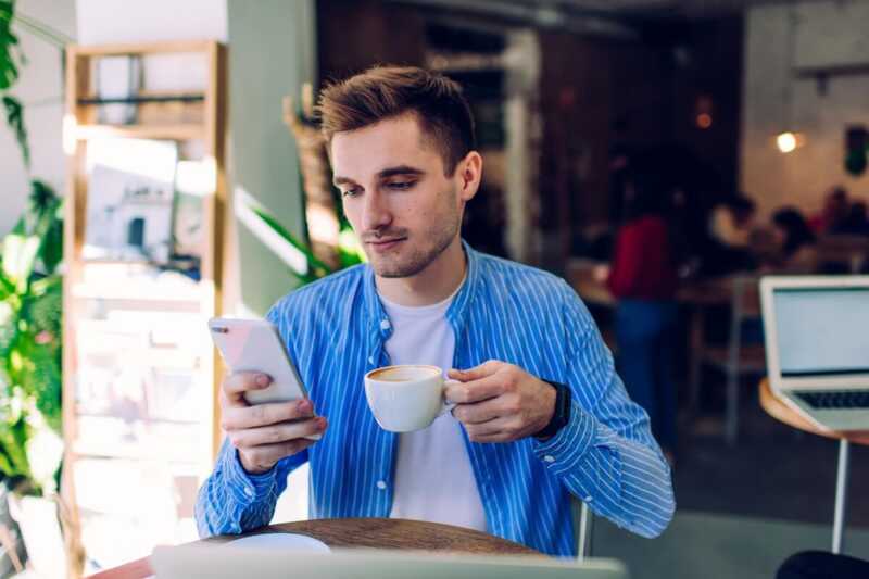 Un homme avec une chemise bleu regarde son téléphone sur une terrasse