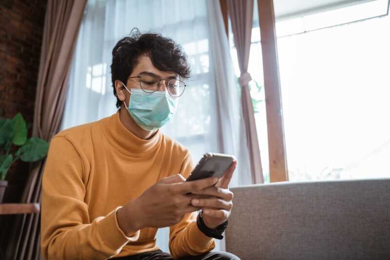 Un jeune homme masqué consulte son téléphone mobile pendant le confinement