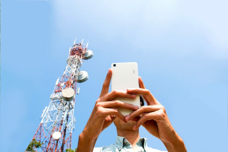 Un homme utilise son smartphone au pied d'une antenne de téléphone mobile